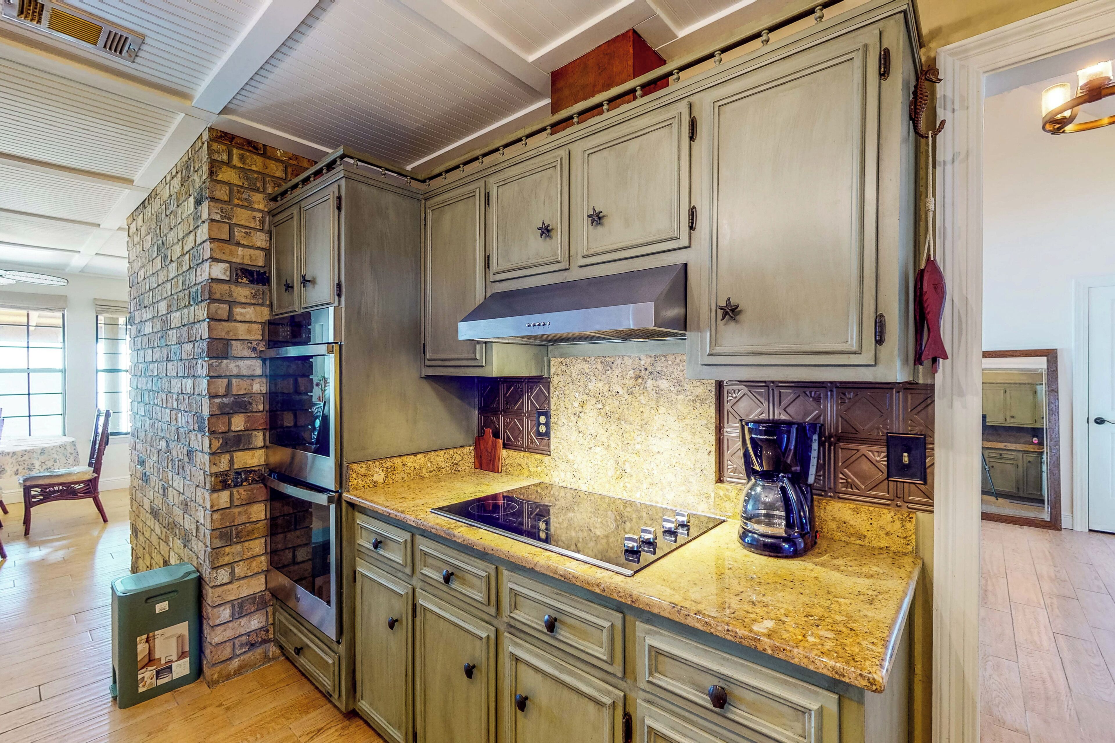 Cocina con pared de ladrillo, encimera de granito, electrodomésticos de acero inoxidable y armarios de madera.