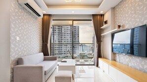 Un salón moderno con sofá, una mesa de centro, televisor y un balcón con vistas a la ciudad.