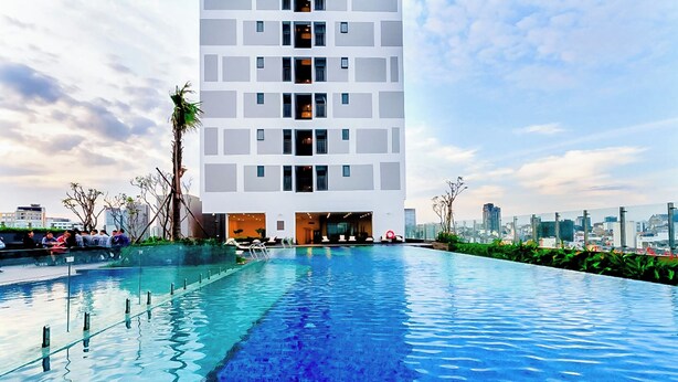 Un edificio moderno con piscina, rodeado de vegetación y un paisaje urbano al fondo.