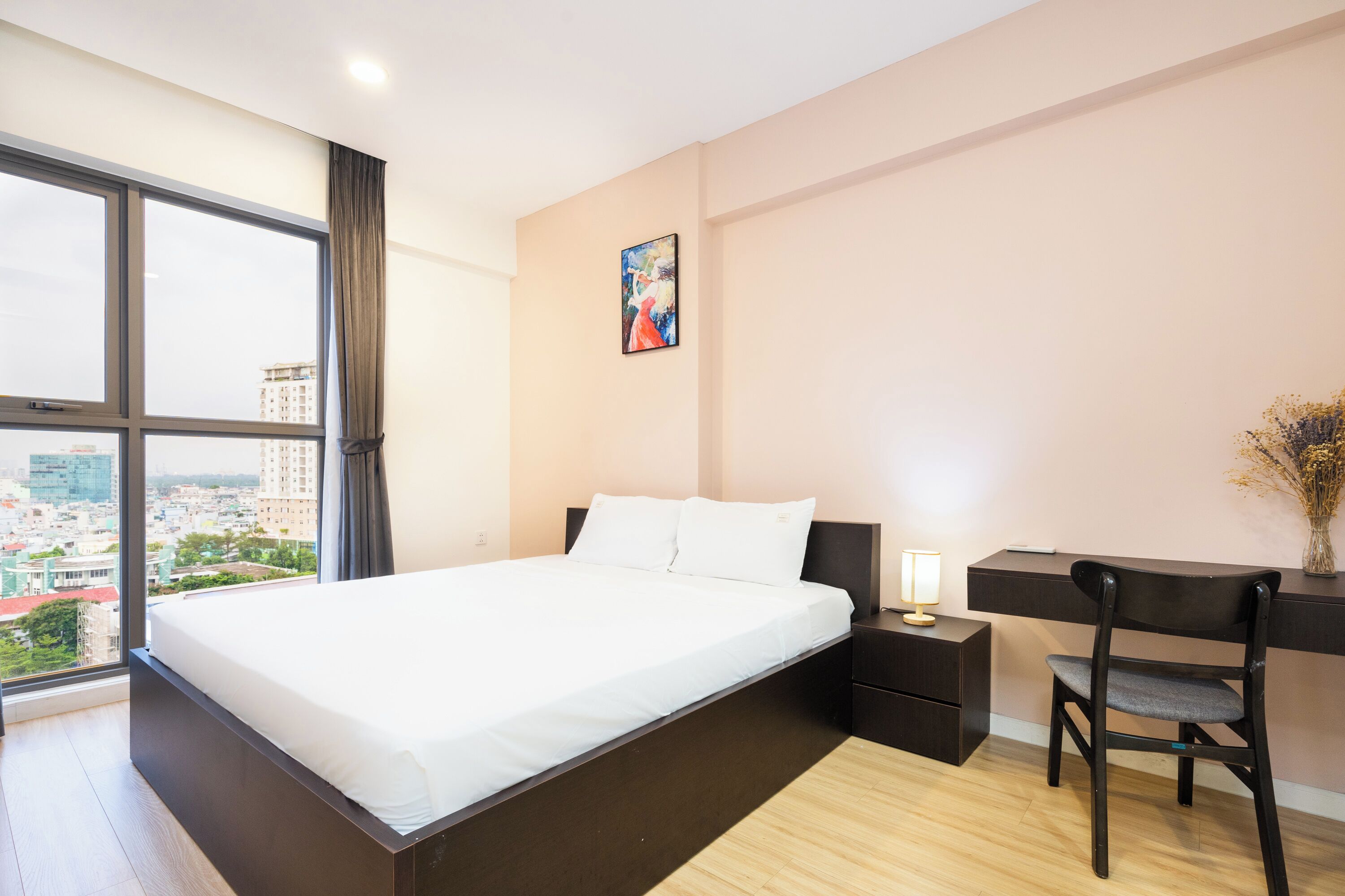 A modern hotel room with a large bed, a desk, a chair, and a window offering a city view.