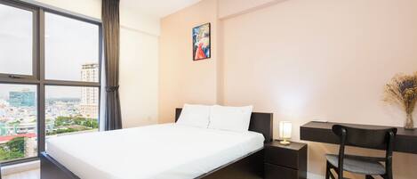 A modern hotel room with a large bed, a desk, a chair, and a window offering a city view.