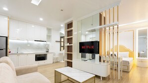 Una sala moderna con sofá, una mesa de centro, televisor, zona de cocina y un dormitorio con cama y mesita de noche.
