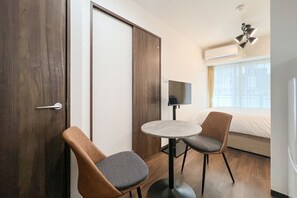 A hotel room with a bed, a TV, a small round table, two chairs, and a door. - Valore Kitahorie (Osaka)