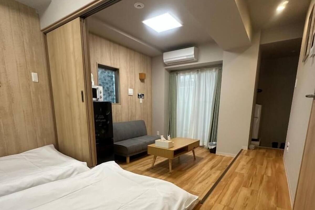 A hotel room with two beds, a sofa, a coffee table, an air conditioning unit, and a window with curtains.
