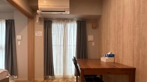 Een hotelkamer met een houten vloer, een eettafel met stoelen, een bed en een airconditioner.