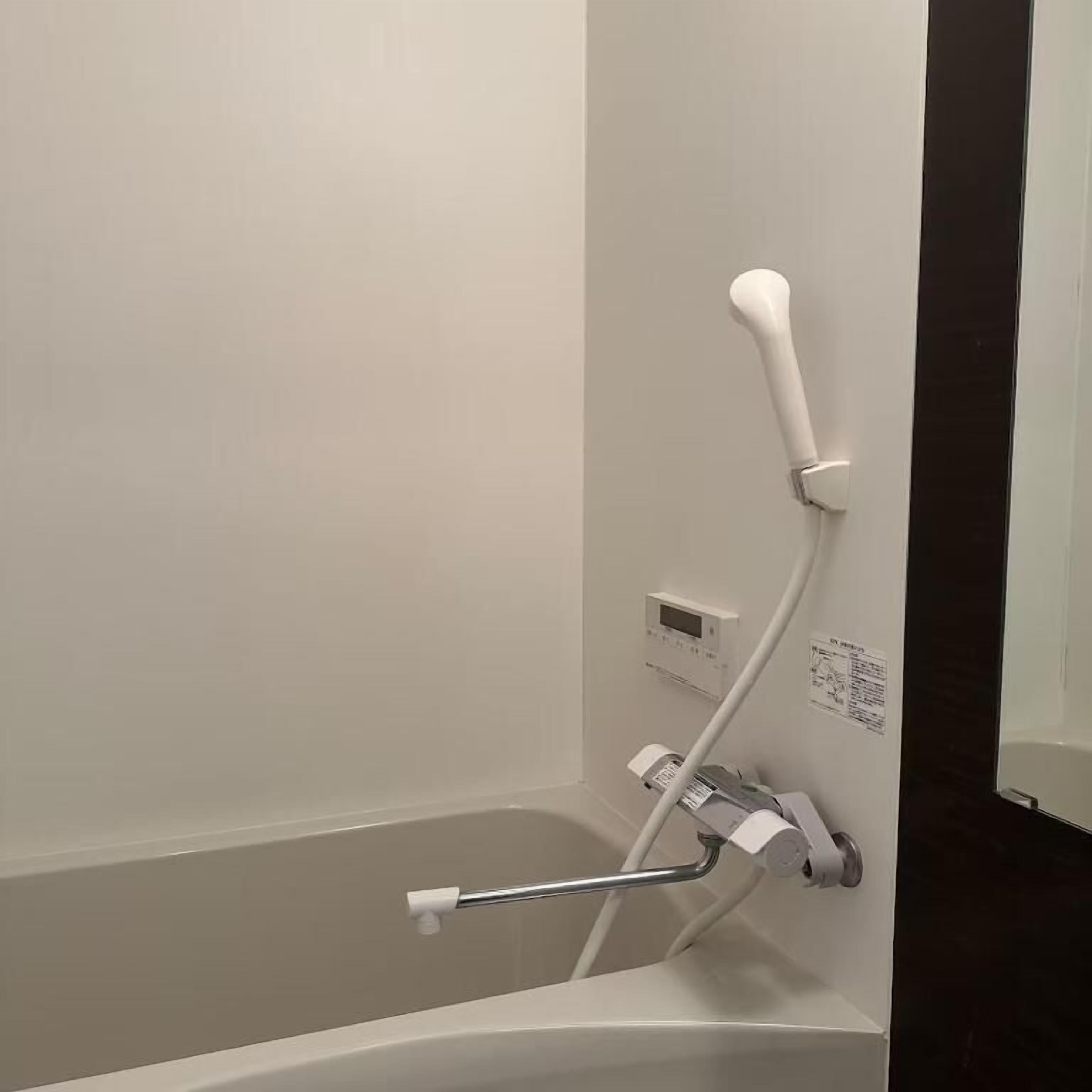A bathtub with a handheld showerhead, a control panel, and a towel rack.