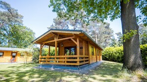 Uma cabana de madeira com varanda, rodeada por árvores e grama.