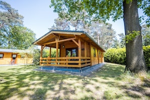 A wooden cabin with a porch, surrounded by trees and grass. - Forest Villa in Markelo With Sunny Garden (Markelo)