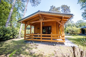 Une cabane en bois dotée d’un porche, entourée d’arbres et d’une zone herbeuse.