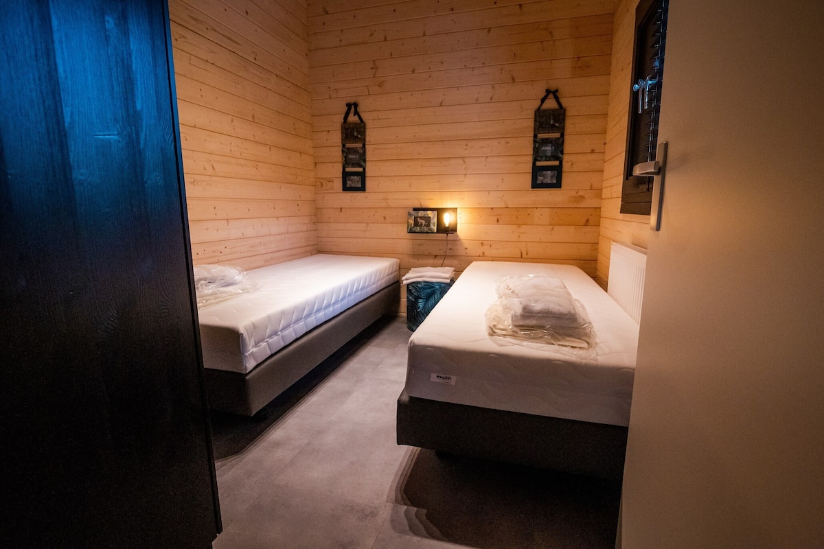 Una habitación pequeña y acogedora con dos camas, paredes de madera y un estante con adornos.