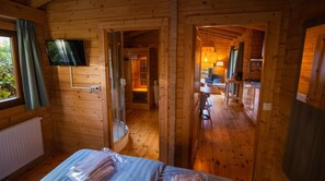 Une cabane en bois avec un lit, un téléviseur fixé au mur et une petite kitchenette.