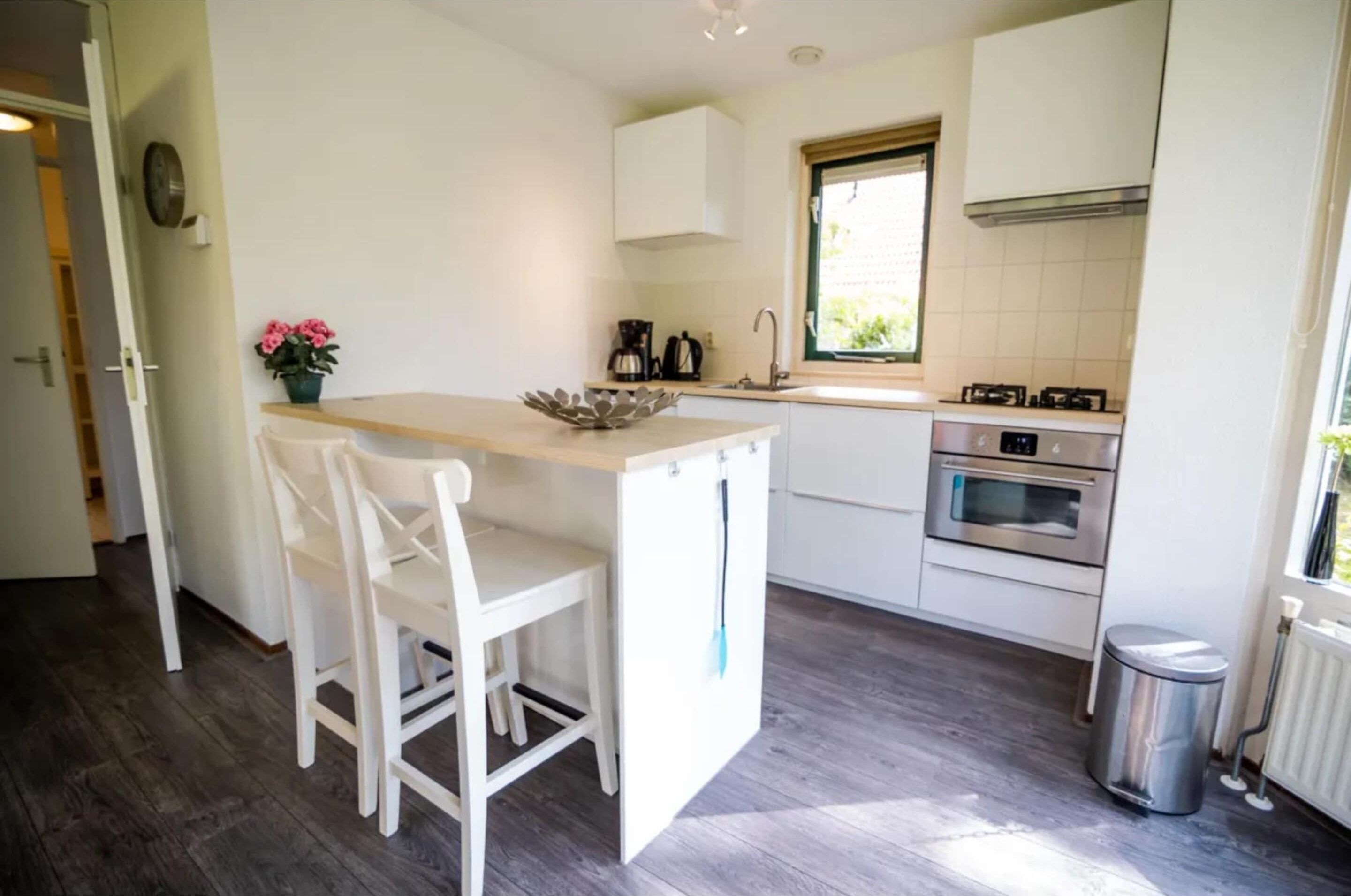 A compact kitchen with white cabinetry, a small dining area with two chairs, a window, and a built-in oven.