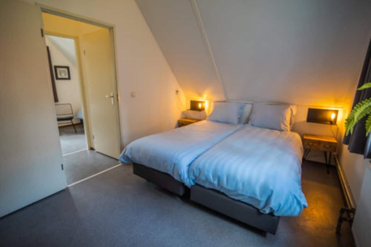Un dormitorio con cama, mesitas de noche y una puerta que da a otra habitación.