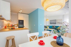 Eine moderne Küche mit weißen Schränken, einer blauen Akzentwand und einem Essbereich mit weißen Stühlen und einem Tisch.