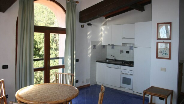A kitchen with white cabinets, a stove, and a sink. There is a dining table with chairs. - Holiday Residence La Cota Quinta, Rio Nell"elba (Rio)