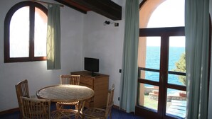 A room with a round table, chairs, a television, and a view of the sea through large windows. - Holiday Residence La Cota Quinta, Rio Nell"elba (Rio)
