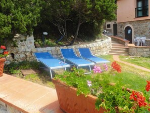 A patio with two blue sun loungers, a stone wall, and a small outdoor seating area with white chairs. - Holiday Residence La Cota Quinta, Rio Nell"elba (Rio)