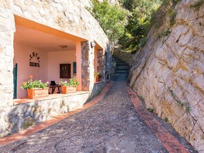 Ein schmaler Steinweg führt zu einem Gebäude mit einer Steinauffahrt und einem Schild, auf dem 