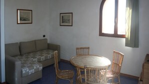 A room with a sofa, a round table with chairs, and two framed pictures on the wall. - Holiday Residence La Cota Quinta, Rio Nell"elba (Rio)