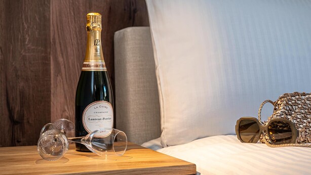 Een fles champagne, twee wijnglazen en een paar zonnebrillen op een nachtkastje.