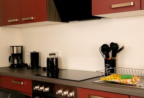A kitchen with a black countertop, stainless steel appliances, and red cabinets.