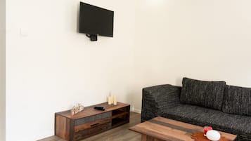 A living room with a dark grey sofa, a wooden coffee table, and a TV mounted on the wall.