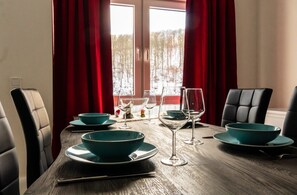 A dining table set with teal bowls and wine glasses, red curtains, and a view of a snowy landscape through a window. - Family Comfort in Guntersberge (Harzgerode)