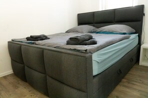 A bed with a grey upholstered headboard, grey bedding, and a blue accent pillow. - Family Comfort in Guntersberge (Harzgerode)