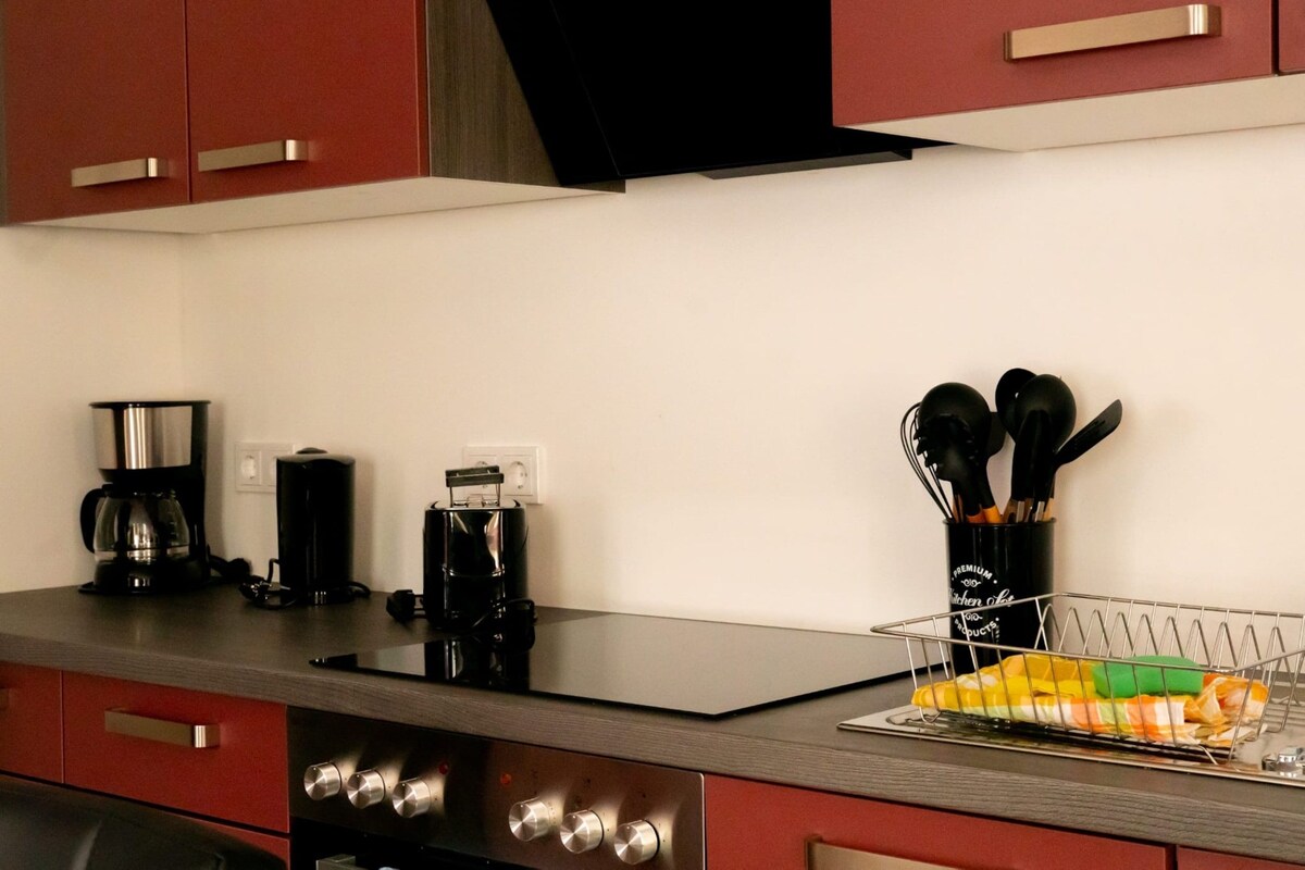 A kitchen with a black countertop, stainless steel appliances, and red cabinets.