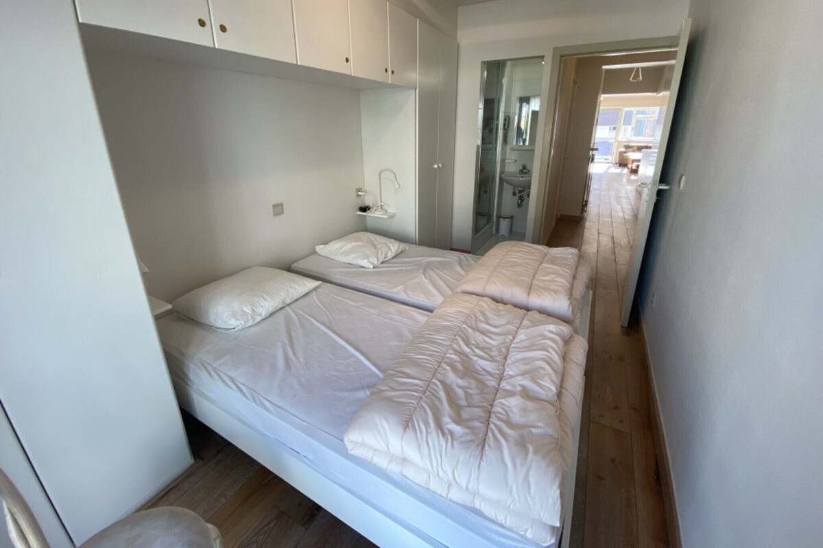 A small, compact bedroom with two single beds, a bedside table, and a wardrobe.