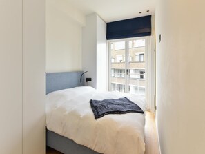A bedroom with a bed, a window, and a view of buildings outside. - Sunny Escape at Albert Beach (Knokke-Heist)
