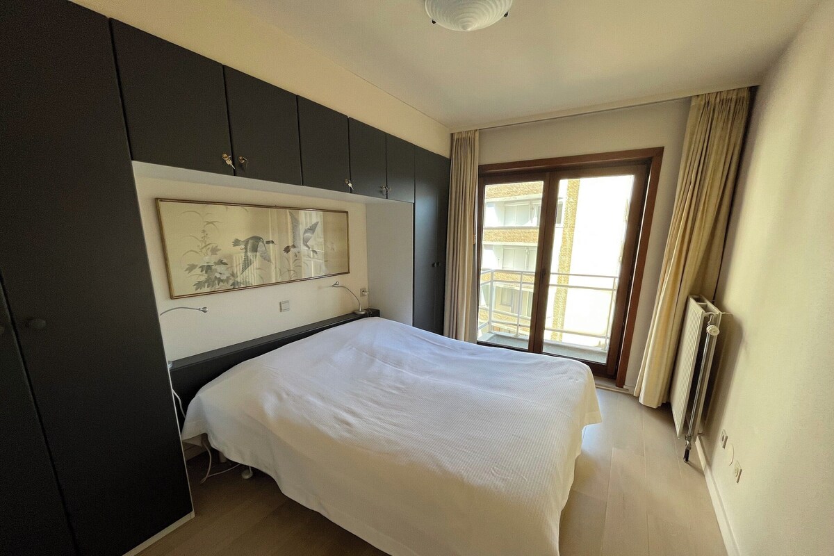 A bedroom with a bed, a large window, a radiator, and a wall-mounted artwork.