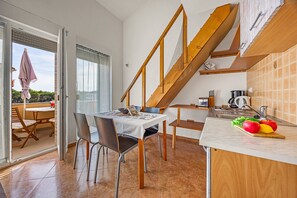A dining area with a table and chairs, a kitchen with a sink and countertop, and a wooden staircase. - Apartment Near Pula With Sea View Balcony (Medulin)