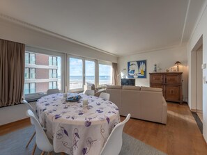 A modern living room with a round dining table, white sofa, and large windows offering a view of the sea. - Modern Seaside Escape (Knokke-Heist)