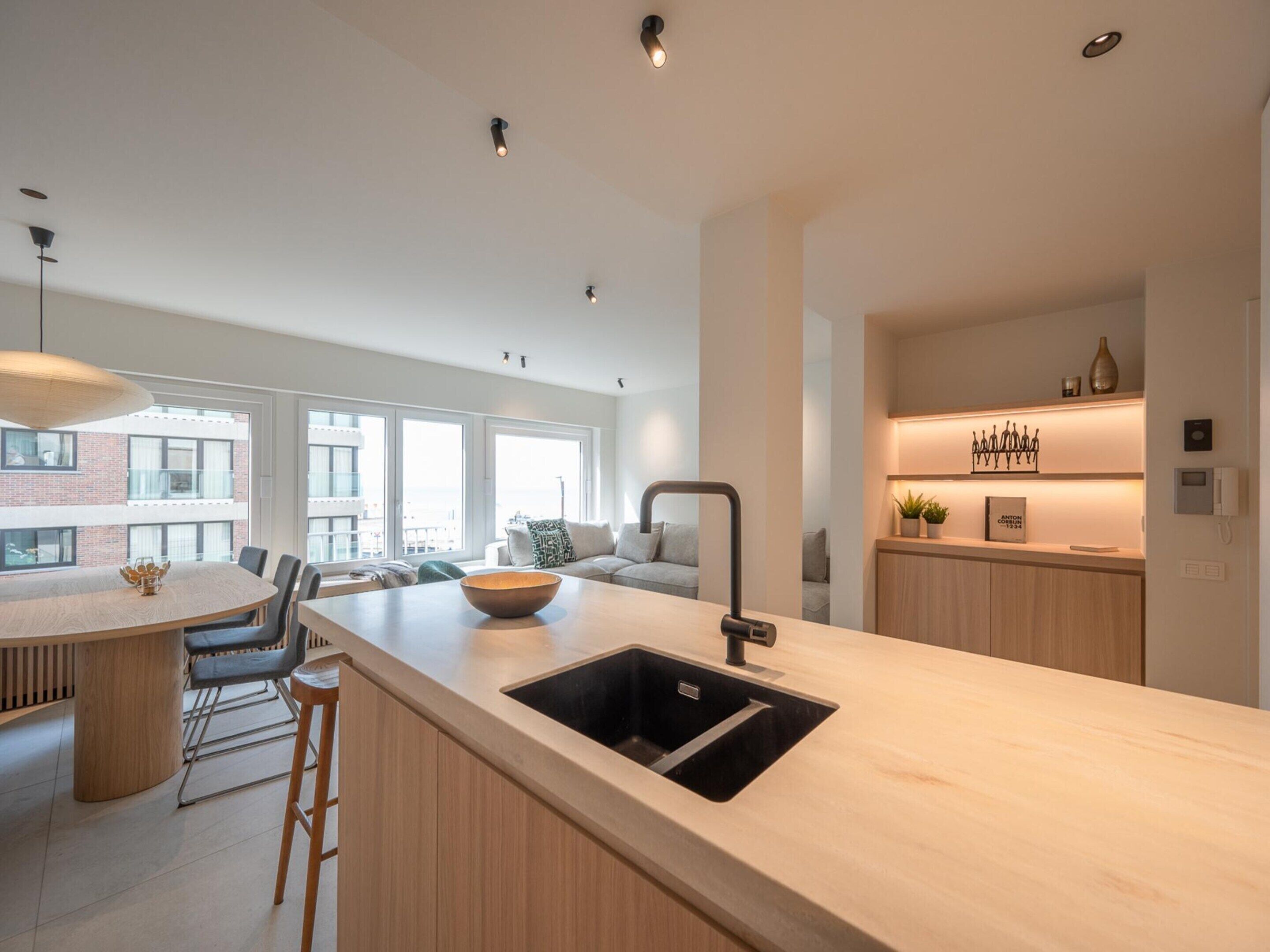 A modern kitchen with a central island, a built-in sink, and a dining area with chairs.