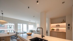 A modern kitchen with a central island, a built-in sink, and a dining area with chairs. - Modern Seaside Escape (Knokke-Heist)