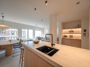 A modern kitchen with a central island, a built-in sink, and a dining area with chairs. - Modern Seaside Escape (Knokke-Heist)