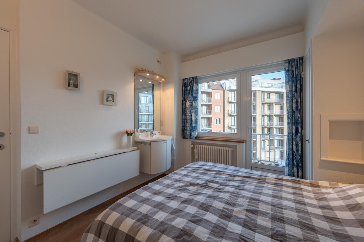 A bedroom with a bed, a window with curtains, a radiator, and a small picture on the wall.