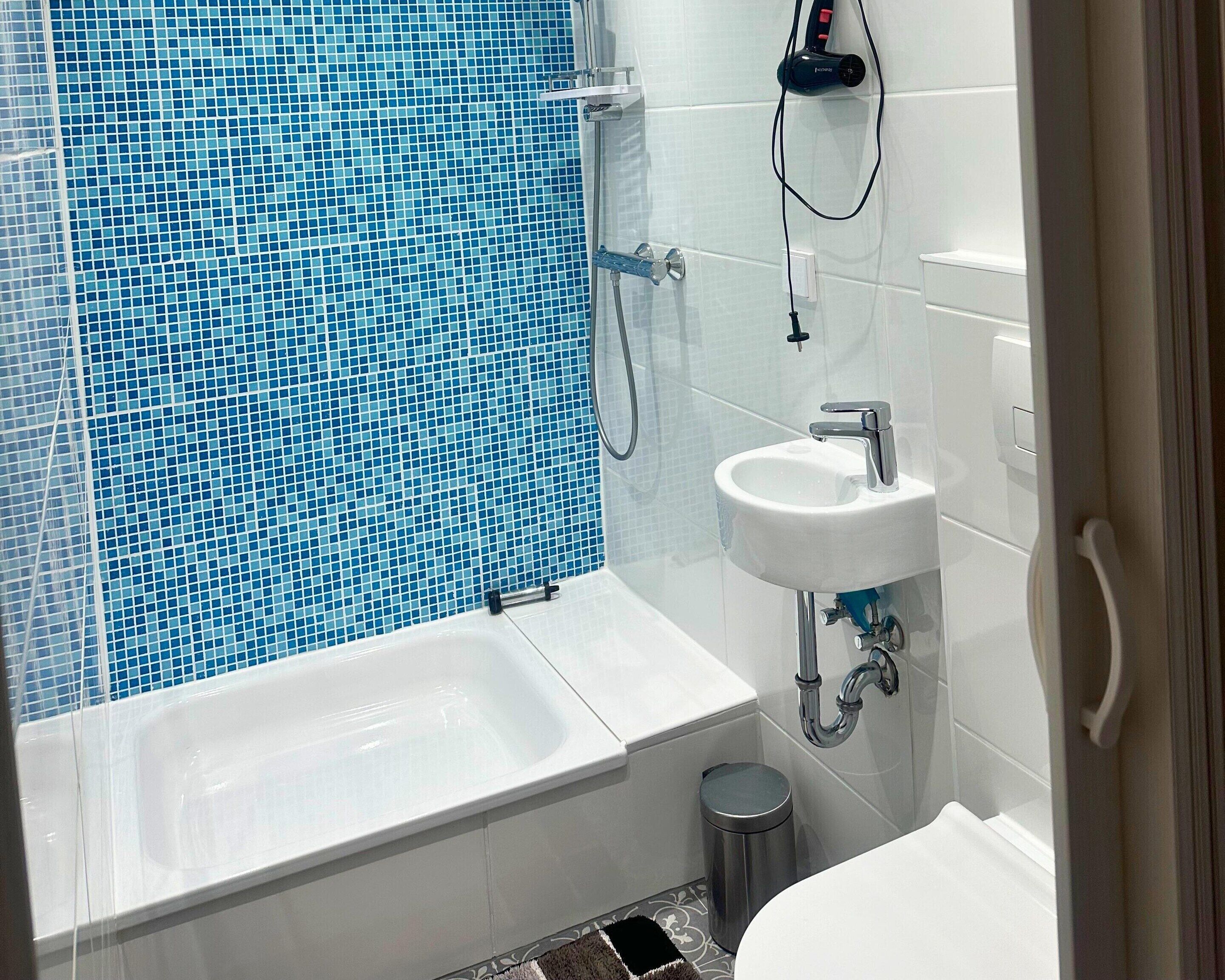 Une salle de bain avec une baignoire, un lavabo et un espace douche aux carreaux de mosaïque bleus.