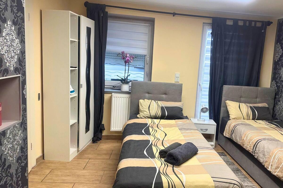 Ein Schlafzimmer mit zwei Betten, einem Kleiderschrank, einem Heizkörper und einem Fenster mit Vorhängen.