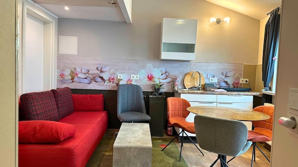 A compact living space with a sofa, chairs, a small table, a kitchen area, and a decorative wall. - Apartment in Pellingen Near Trier (Trier)