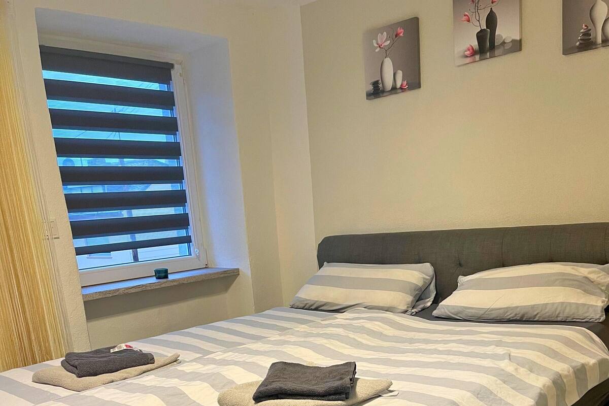 Ein Schlafzimmer mit einem Bett, zwei Kissen, einem Fenster mit Jalousien und drei Wandbildern.