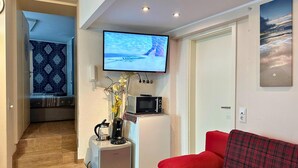 Un espacio habitable compacto con una televisión instalada en la pared, un refrigerador pequeño, un microondas y un sofá rojo.