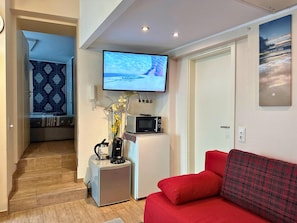 Ein kompakter Wohnraum mit an der Wand befestigtem Fernseher, kleinem Kühlschrank, Mikrowelle und einem roten Sofa.