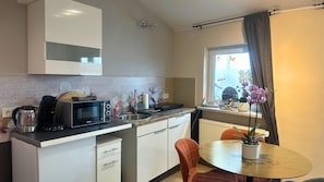 A compact kitchen with a microwave, kettle, and sink. There's a window with curtains and a small table with a chair. - Apartment in Pellingen Near Trier (Trier)