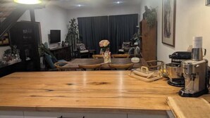 Un espace repas comprenant une table en bois, des chaises, une machine à café et des lampes suspendues.