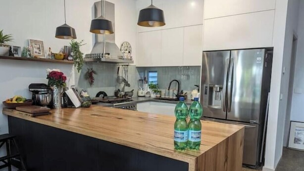 Une cuisine moderne dotée d’un îlot central en bois, d’appareils électroménagers en acier inoxydable, de luminaires suspendus et d’un crédence noire.