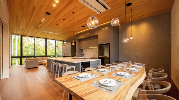 A modern kitchen with a wooden island, large windows, and a dining area with a long table set for six. - Yuzen (Kutchan)