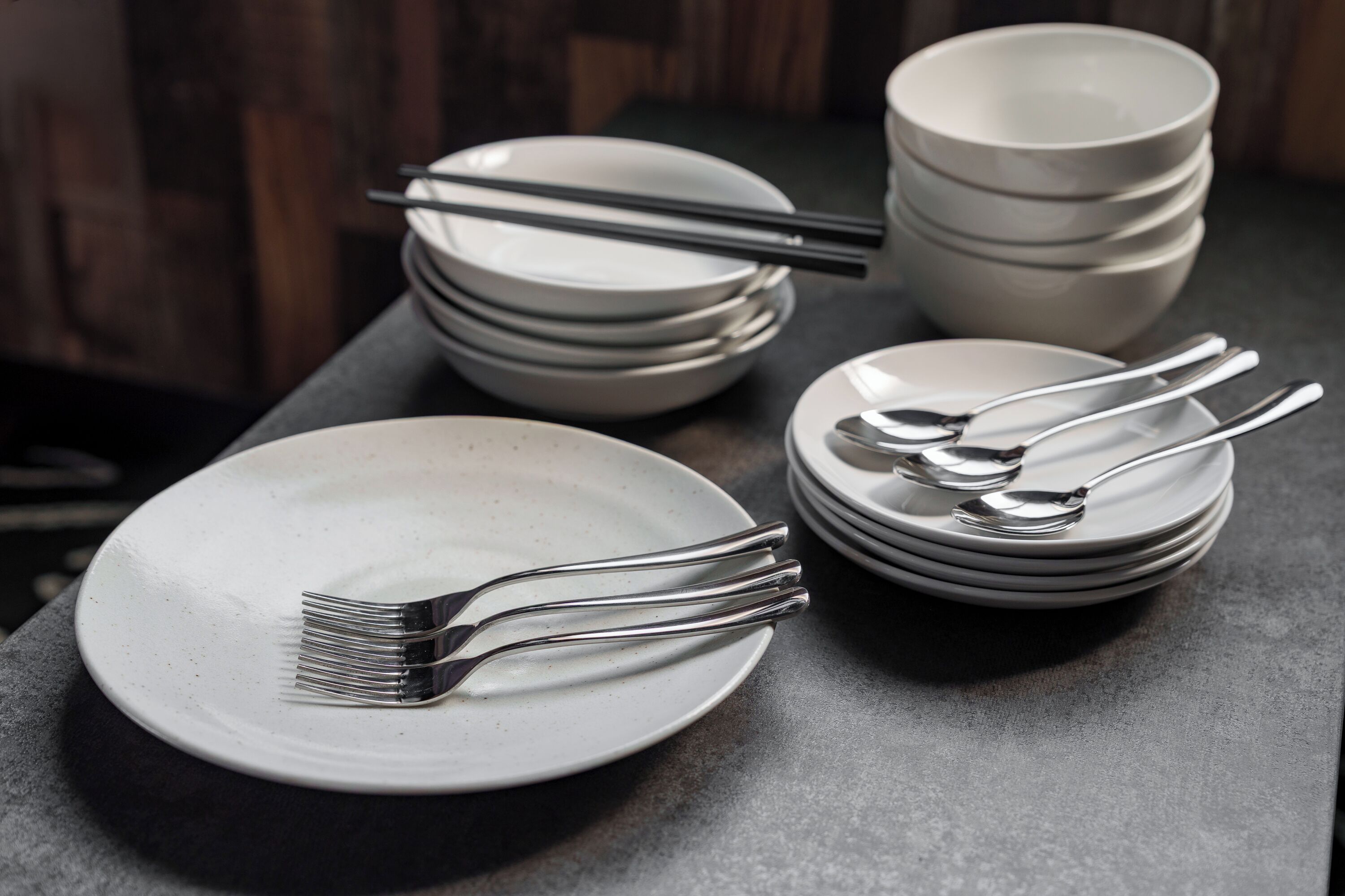 A stack of white plates and cutlery on a dark surface.
