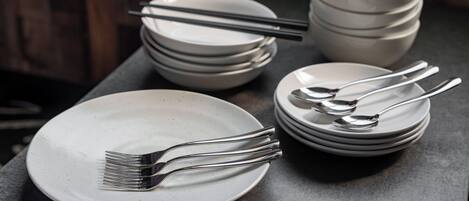 A stack of white plates and cutlery on a dark surface.